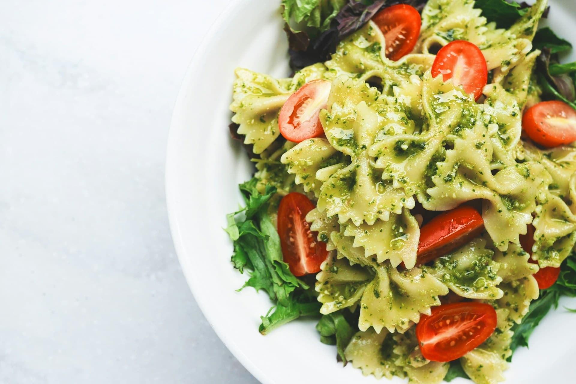 Pesto pasta with tomatoes and greens on a white plate